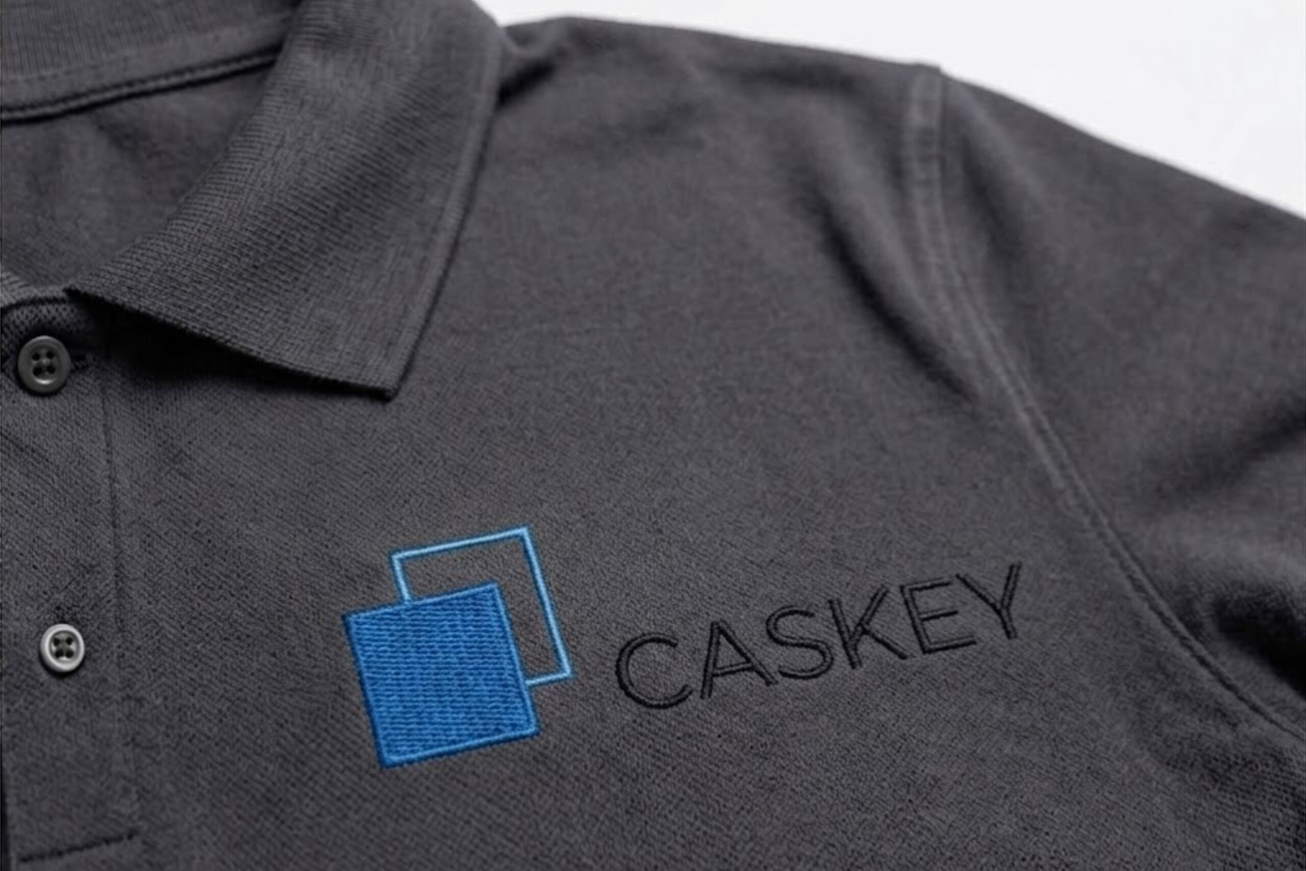 Close-up of a custom embroidered Caskey logo on a black corporate polo shirt showcasing branded apparel and professional embroidery.