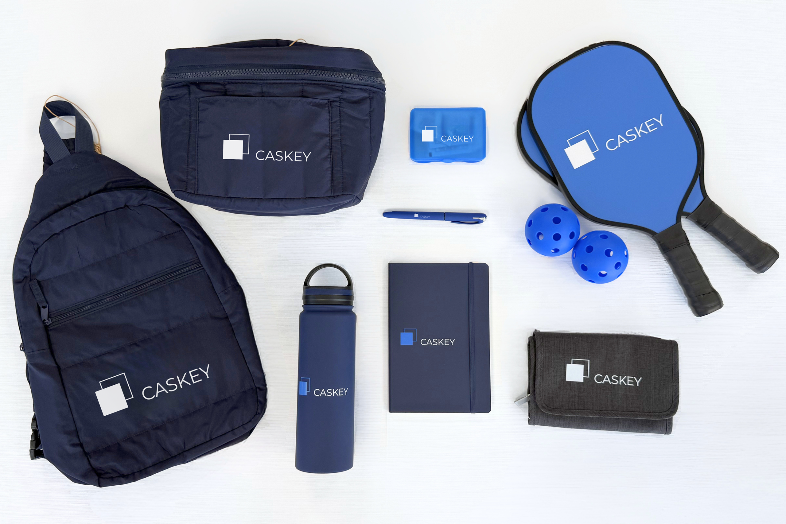 Caskey promotional products including branded bags, drinkware, notebook, pen, and pickleball set.