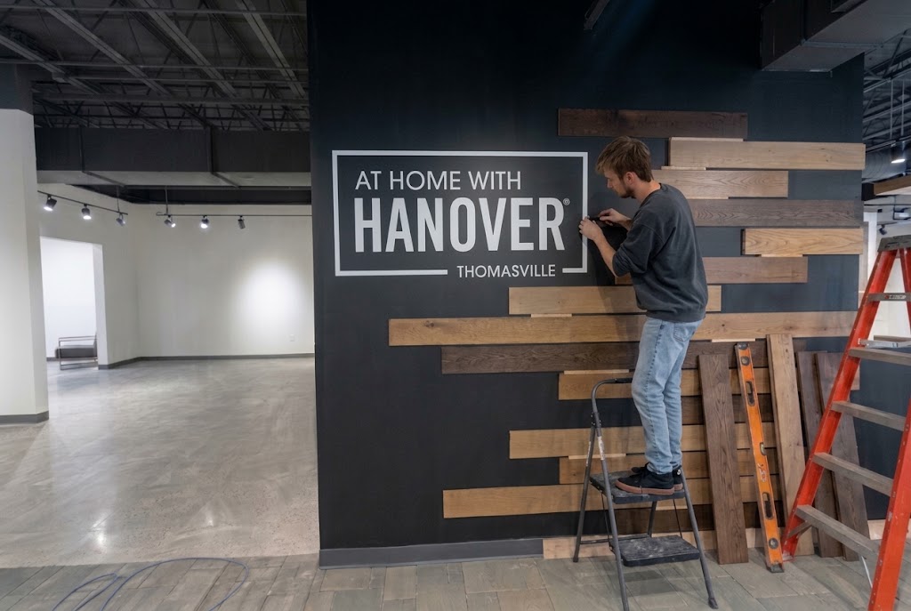 Installer applying large format graphics reading “At Home with Hanover” to a showroom wall accented with wood panels.
